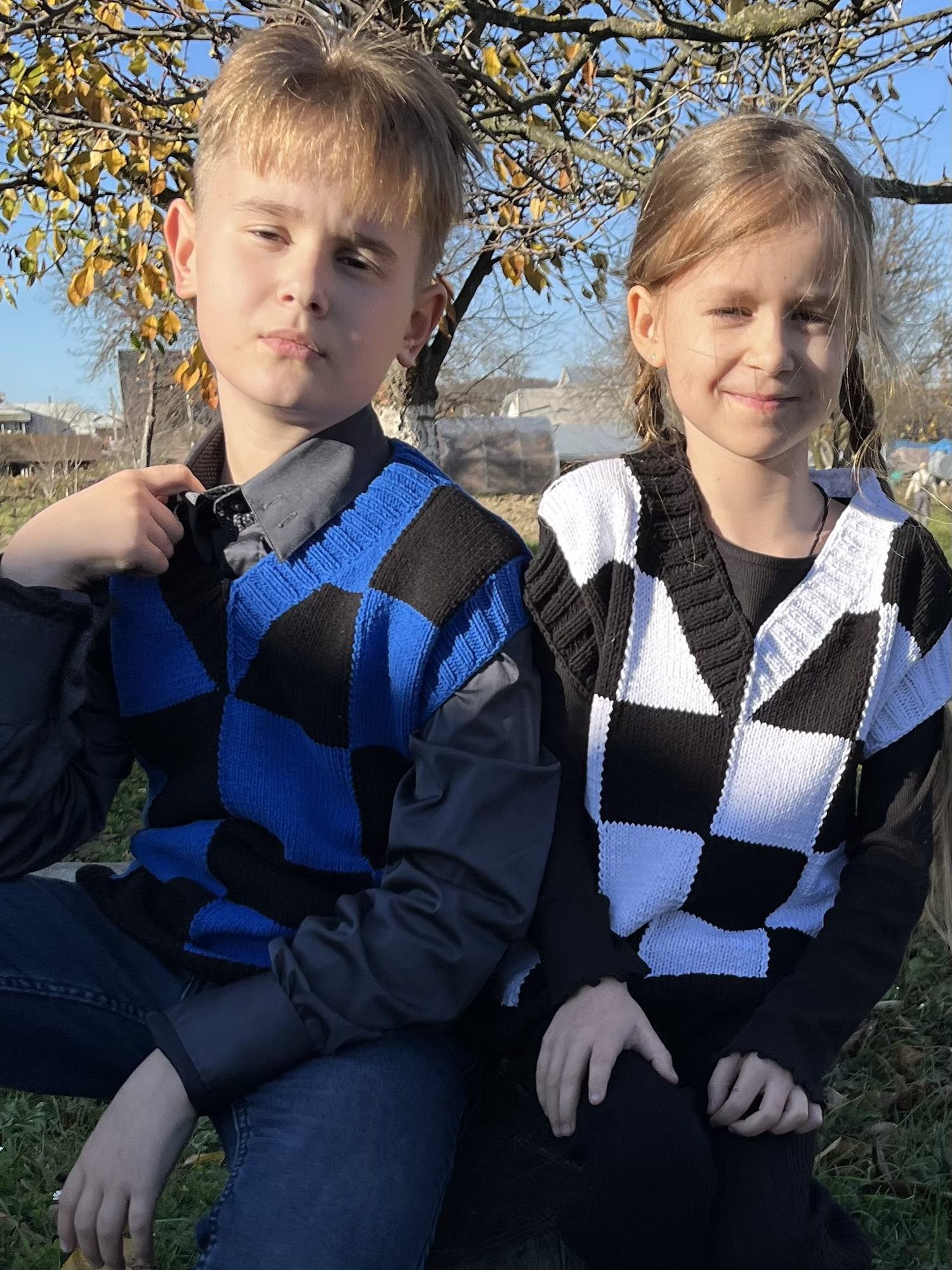 Two children wearing checkerboard intarsia vests